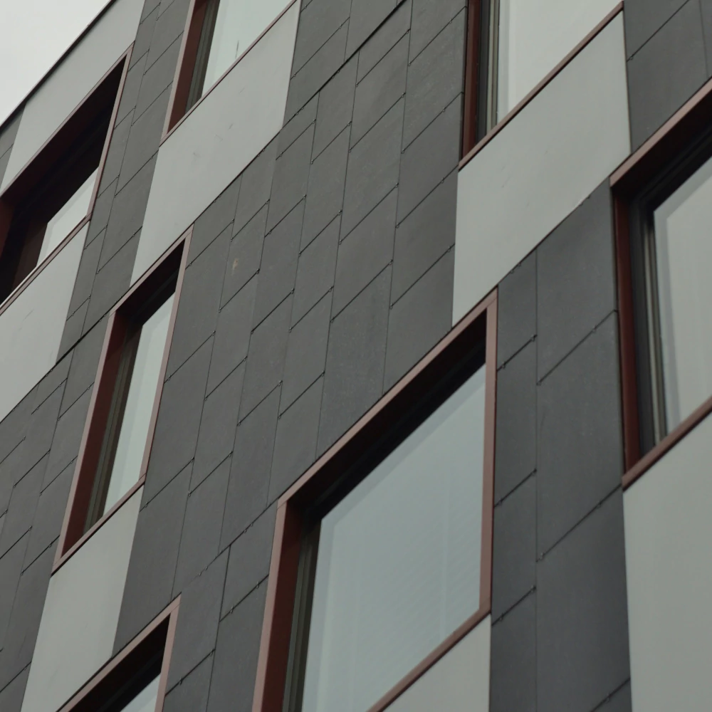 Nowoczesna elewacja budynku wielorodzinnego wykonana z ciemnoszarych i jasnoszarych paneli z widocznymi oknami w brązowych obramowaniach, reprezentująca zasoby spółdzielni mieszkaniowej.